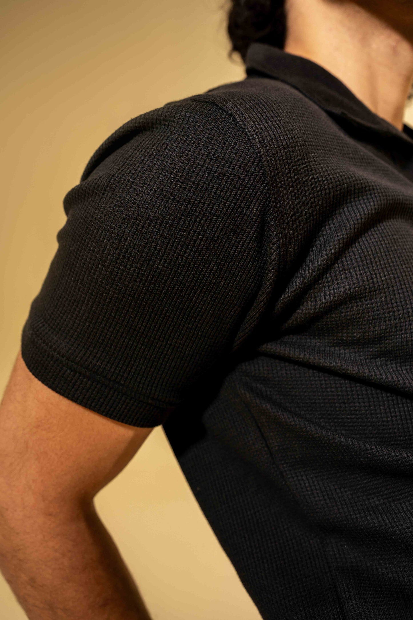 Close-up of a person wearing a black textured shirt against a beige background