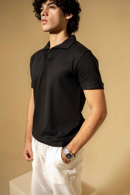 Man wearing a black polo shirt and white pants against a beige background