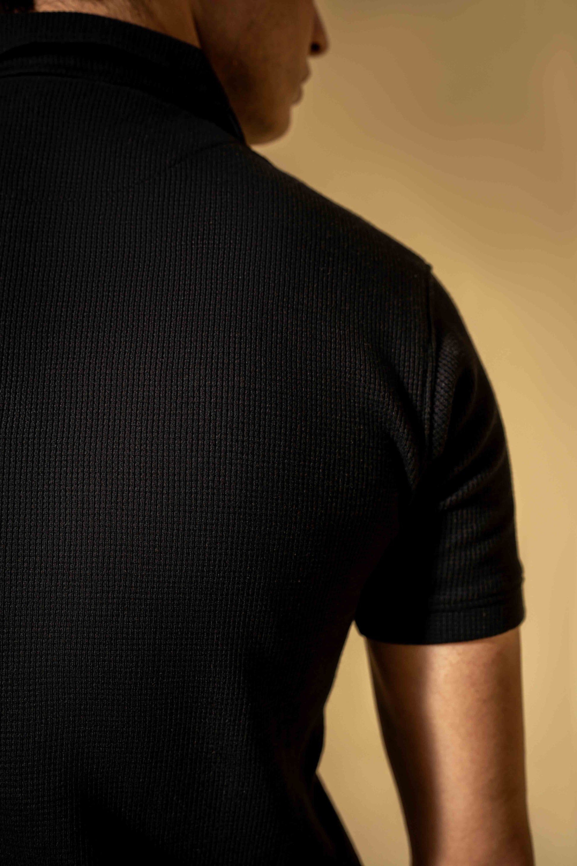 Person wearing a black textured shirt against a beige background