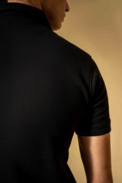 Person wearing a black textured shirt against a beige background