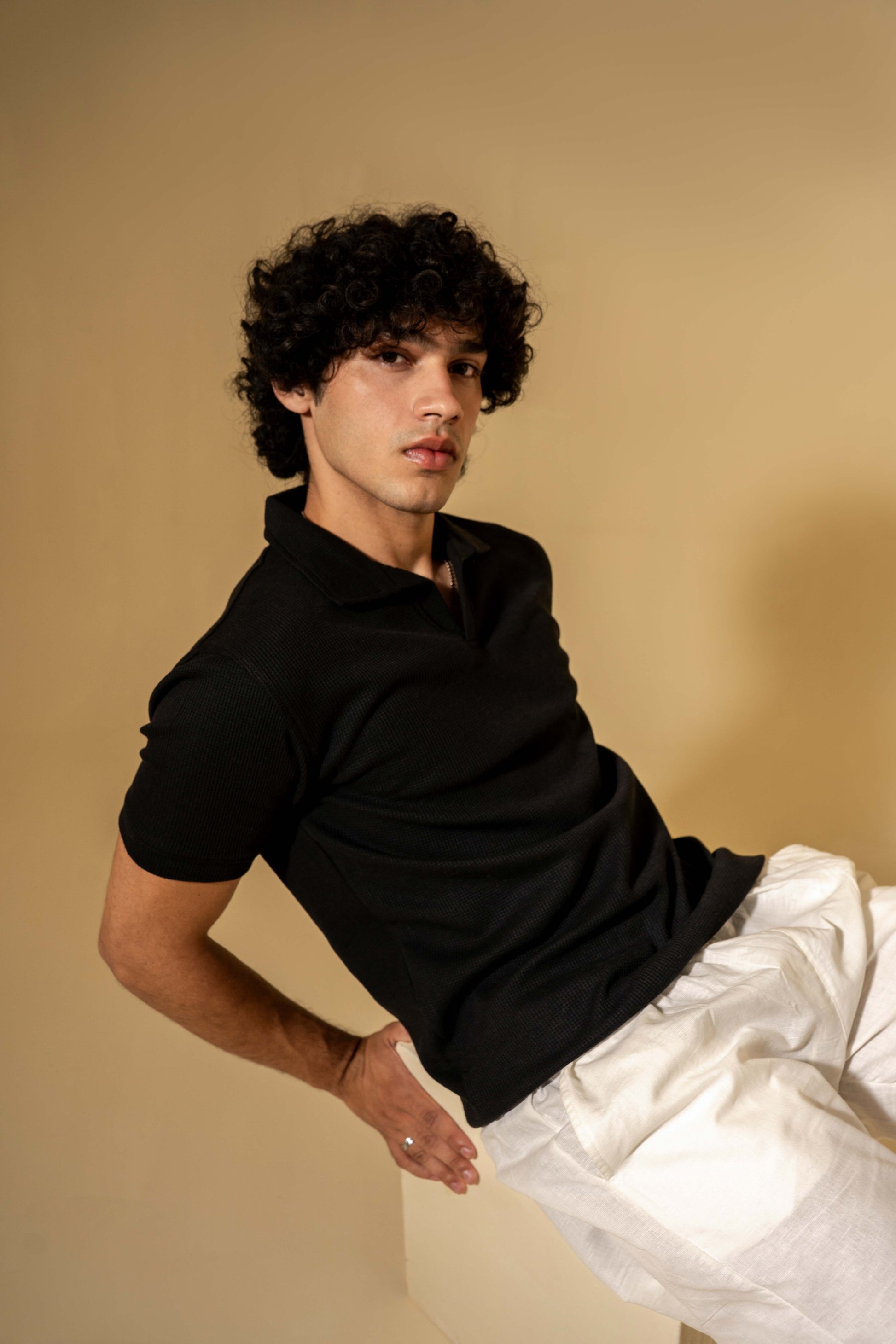 Person wearing a black shirt and white pants against a beige background