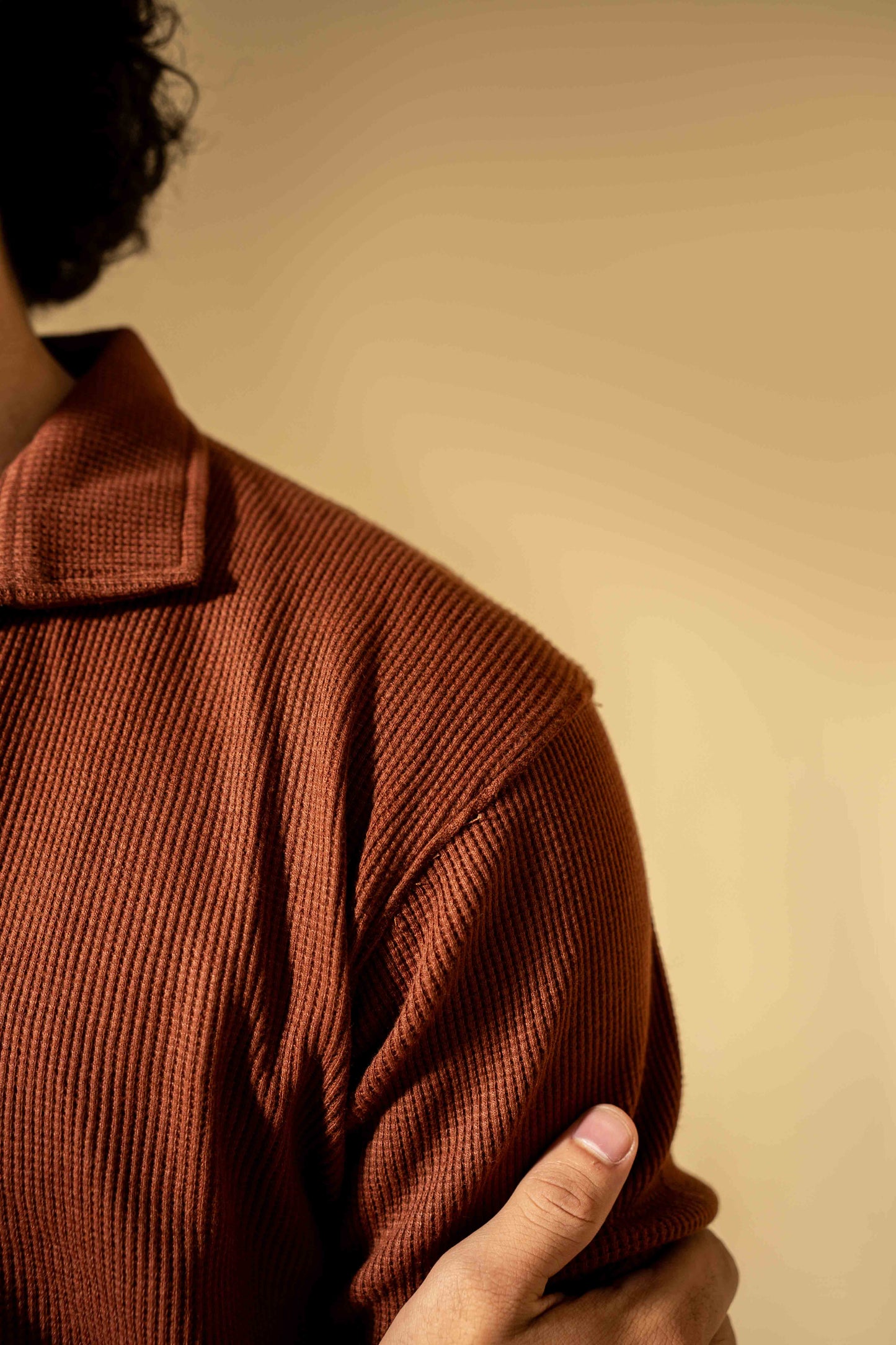 Person wearing a brown textured sweater against a beige background