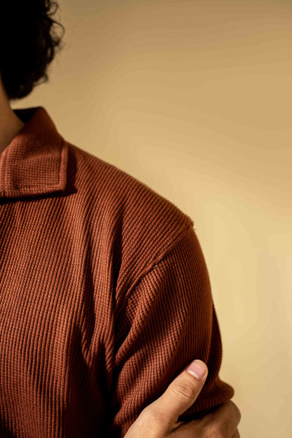 Person wearing a brown textured sweater against a beige background