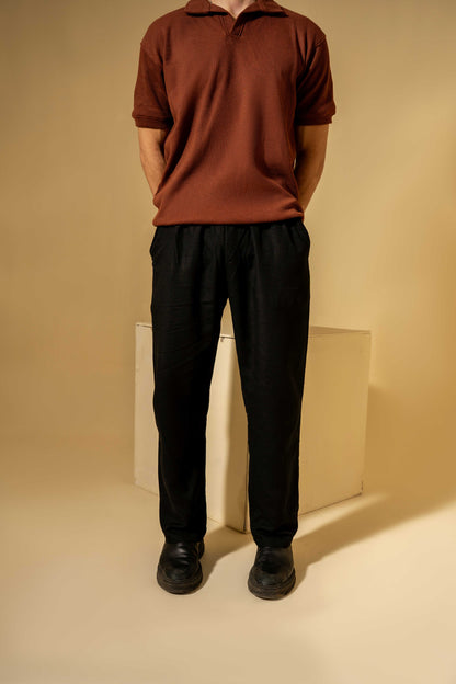 Person wearing a brown polo shirt and black pants standing against a beige background