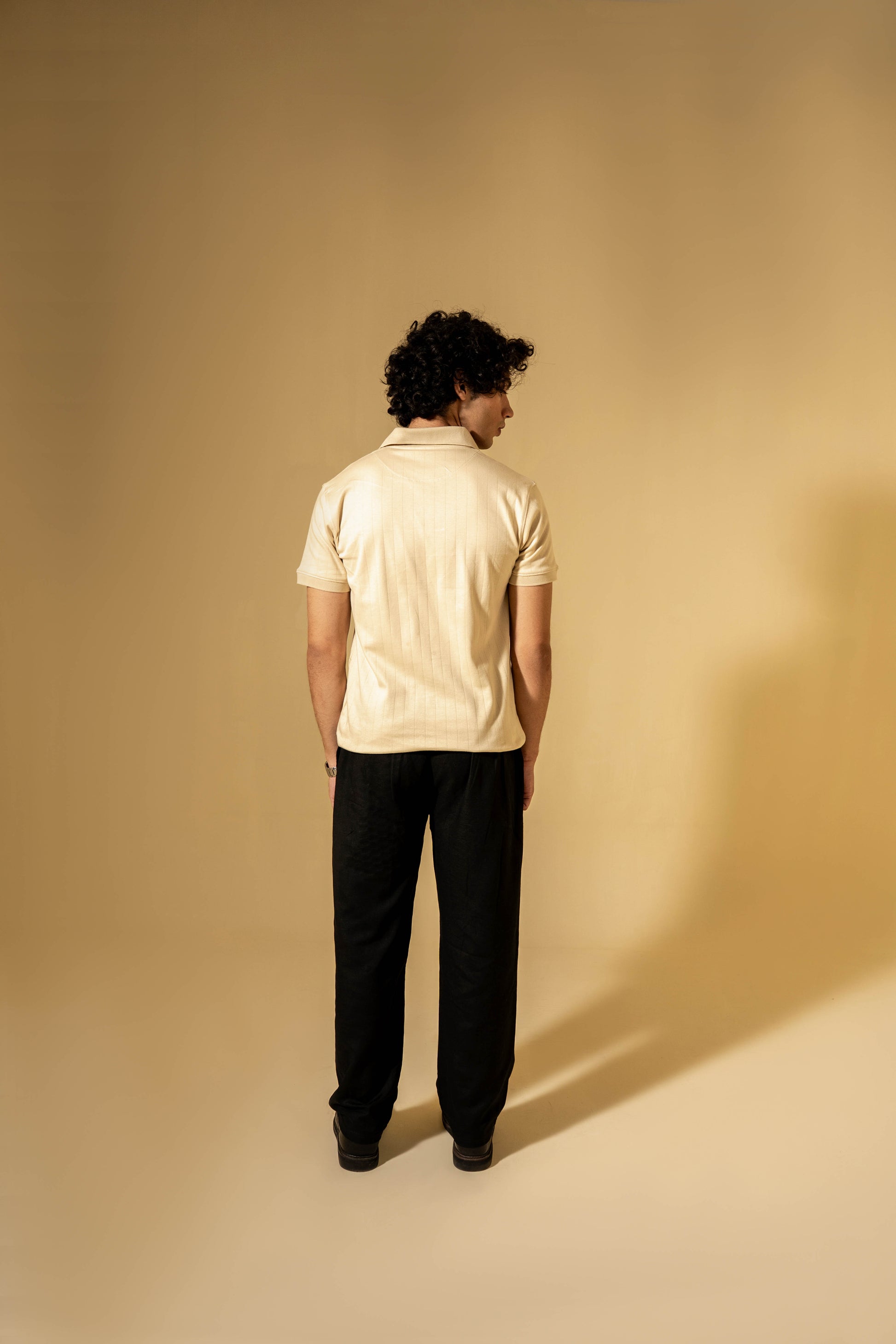 Person wearing a beige polo shirt and black pants against a beige background
