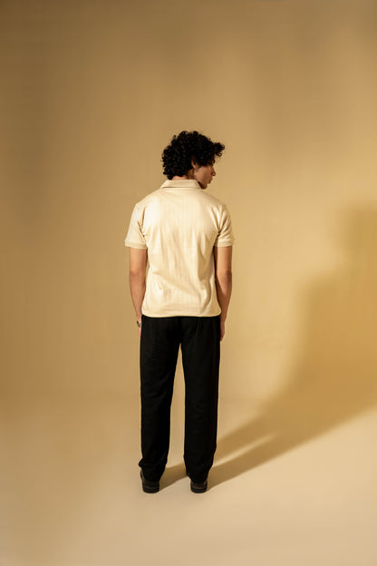 Person wearing a beige polo shirt and black pants against a beige background