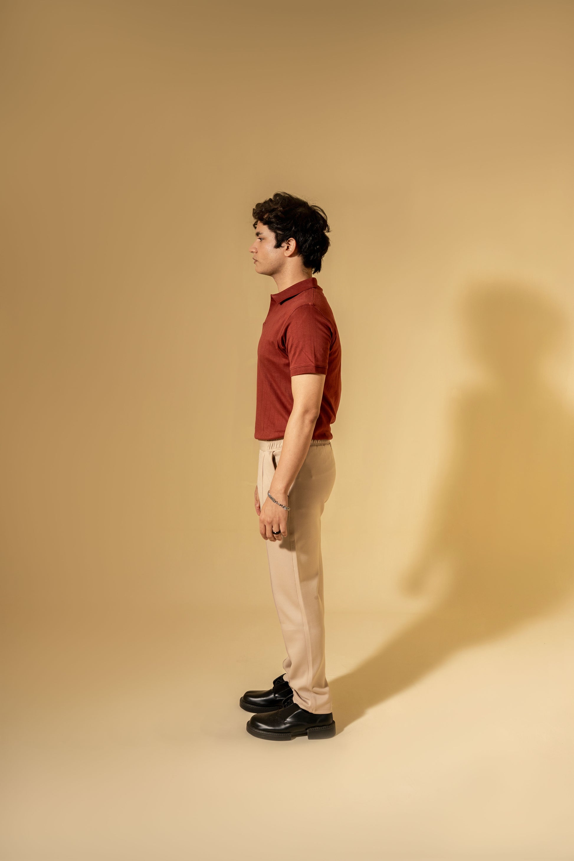 Man wearing a red shirt and beige pants standing against a beige background