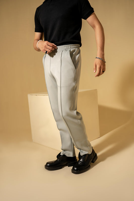 Person wearing light gray pants and black shoes on a beige background