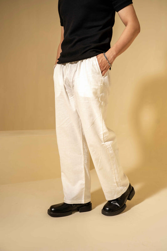 Person wearing a black shirt, white pants, and black shoes on a beige background